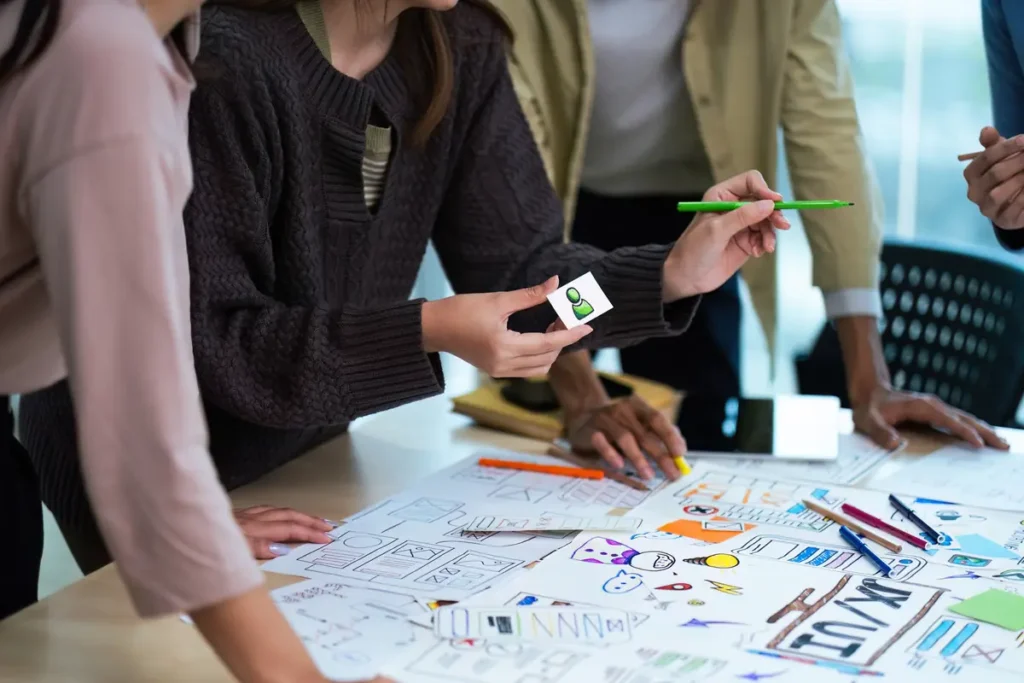 People lean over a table covered with sketches and notes, working on them together.